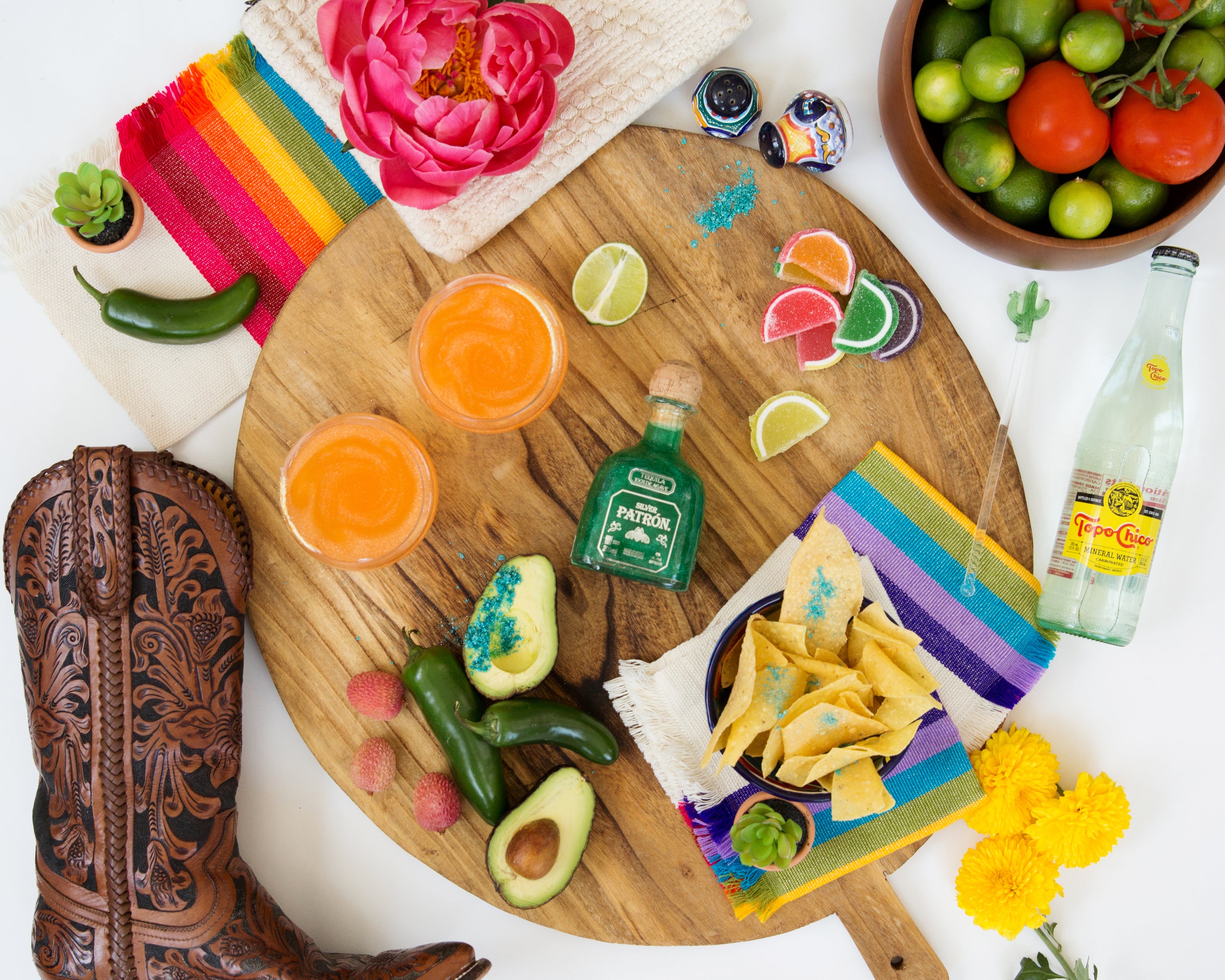 Round charcuterie board with brightly colored striped napkins, avocados, jalapeños, two mango margaritas, colorful candy, Topo Chico, chips and guacamole - all shimmered with Sugar Mama Shimmer